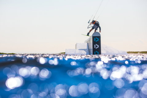 Duotone Gambler kiteboard wake-style durante il wakestyle in un kite park su acqua piatta