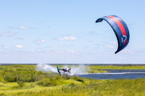 Duotone Gambler wake-style kiteboard durante il kitesurf in un canale costiero di acqua piatta