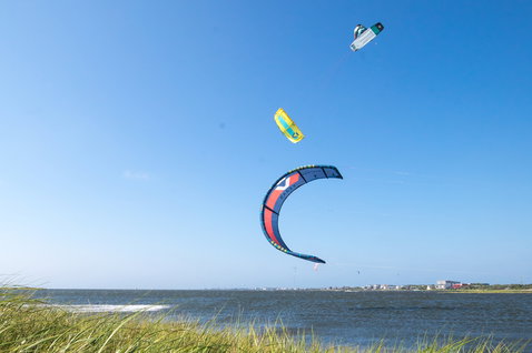 Duotone Vegas LEI kite during kitesurfing at a coastal beach with dune grass and ocean horizon