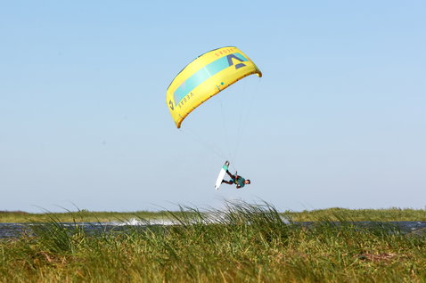 Duotone Team Series Textreme tabla de kitesurf twin-tip durante el kitesurf en costa con dunas y agua