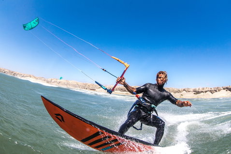 Duotone Neo LEI Kite 9m beim Wellenreiten am Ozeanstrand mit karger Felsküste