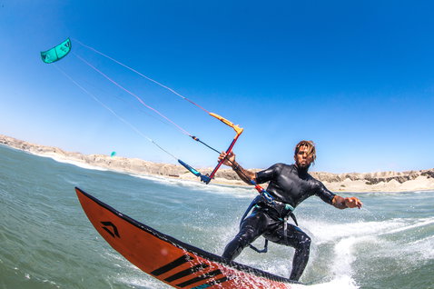 Duotone Wam directional kiteboard during kitesurfing at an ocean beach with arid rocky coastline