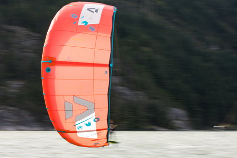 Duotone Evo LEI Kite beim Kitesurfen vor Berg- und Waldkulisse mit verschneitem oder sandigem Untergrund