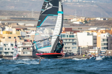Duotone Windsurfing WARP_FOIL foil sail during foiling on the coastal ocean with urban backdrop
