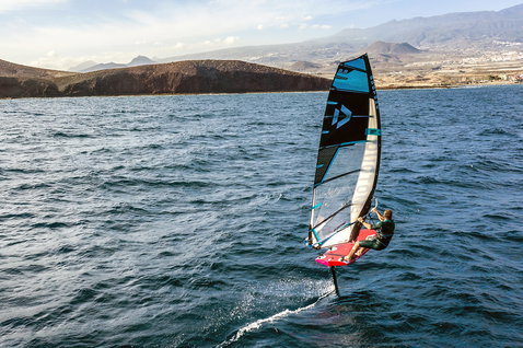 Duotone WARP_FOIL foil sail during foiling on the ocean with volcanic mountains in the background