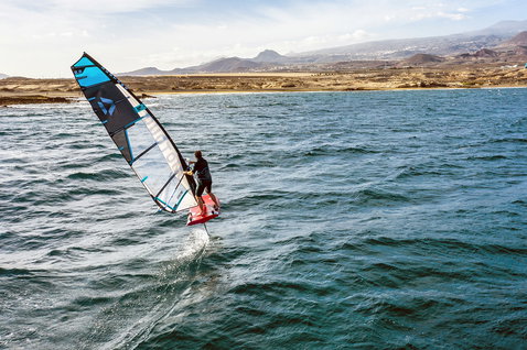 Duotone WARP_FOIL 2021 foil sail during foiling in an ocean bay with arid coastal landscape and mountains in the background