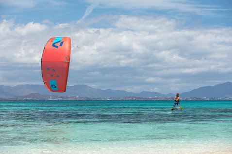 Duotone Mono LEI kite durante foiling en una playa oceánica tropical con montañas al fondo