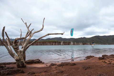 Duotone Juice LEI Kite beim Kitesurfen an einem Binnensee mit roter Erde, Totholz und Bergpanorama