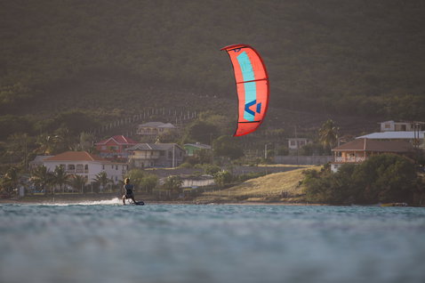 Duotone Juice LEI Kite beim Kitesurfen in einer Küstenbucht mit Bergdorf im Hintergrund
