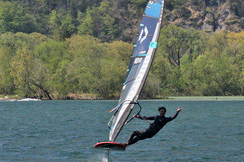 Duotone WARP_FOIL foil sail while foiling on an inland lake with tree-covered hillside