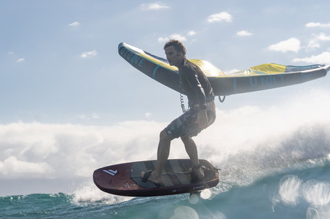 Duotone Unit foil wing durante il wing foiling sull'oceano in grigio, giallo e teal