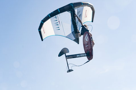 Ala foil Duotone Unit durante wing foiling, rider in volo con foilboard Fanatic su cielo azzurro