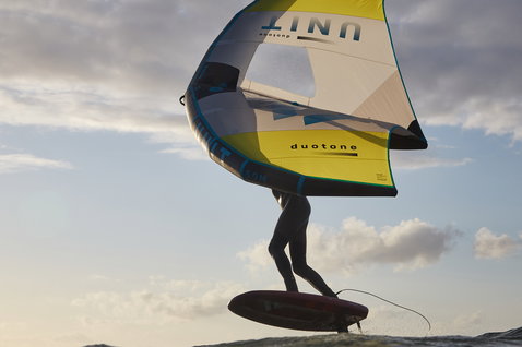 Duotone Unit foil wing durante il wing foiling sull'oceano in grigio scuro e giallo-verde