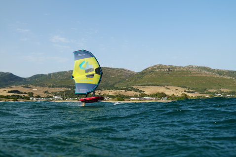 Duotone Unit foil wing durante il wing foiling in mare con colline costiere sullo sfondo