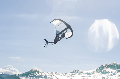 Duotone Unit foil wing durante il wing foiling sopra le onde dell'oceano in blu acciaio e bianco