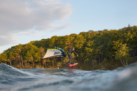 Duotone Unit foil wing durante una sessione di wing foiling su un lago al tramonto con bosco sullo sfondo