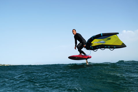 Duotone Unit foil wing durante il wing foiling in mare in blu scuro e giallo lime