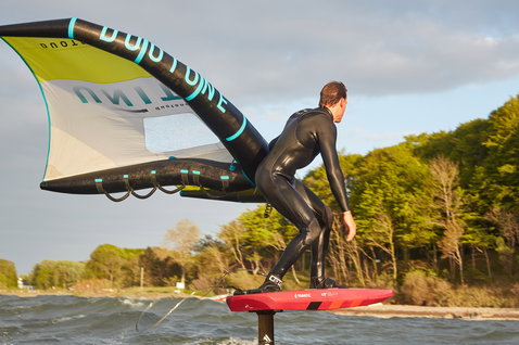 Duotone Unit foil wing durante il wing foiling in costa in oliva, nero e turchese