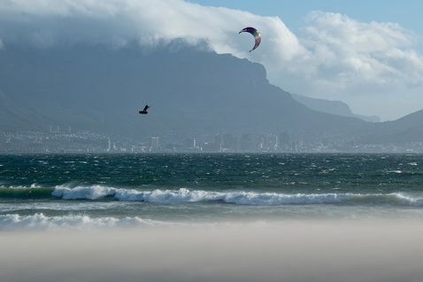 Duotone Dice LEI kite durante il kitesurf sulla spiaggia con montagne e città sullo sfondo