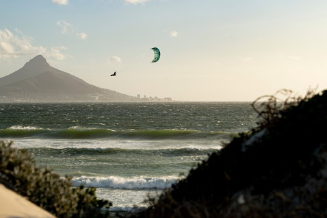 Duotone Dice LEI kite durante il kitesurf sulla spiaggia con sfondo montuoso