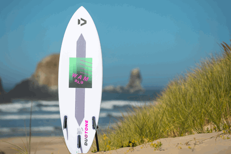 Duotone Wam SLS Wave-Kiteboard in weiß, magenta und grün auf dem Strand mit Sanddünen und Meer