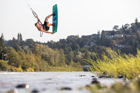 Duotone Spike kiteboard twin-tip durante il kitesurf su un fiume con riva alberata