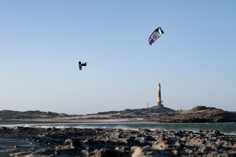 Duotone Evo SLS LEI kite durante el kitesurf en una playa costera con faro y orilla rocosa