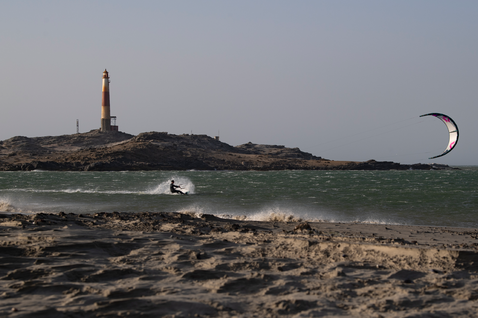 Duotone Evo SLS kite LEI durante el kitesurf en una playa del océano con isla rocosa y faro
