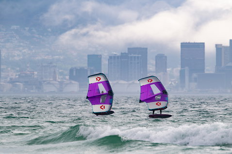Duotone Slick Foilwing beim Wing Foiling auf dem Meer vor städtischer Skyline in violett und hellblau