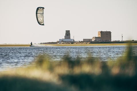 Duotone Juice D/LAB LEI Kite beim Kitesurfen in einer Küstenlagune mit Industriegebäuden im Hintergrund