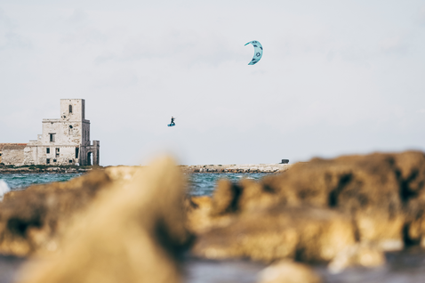 Duotone Vegas kite LEI durante il kitesurf su una costa rocciosa con torre in pietra storica