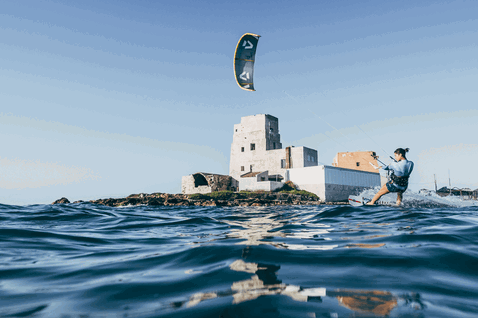 Duotone Gonzales tabla de kitesurf twin-tip durante kitesurf en costa mediterránea cerca de Sicilia con torre histórica en islote