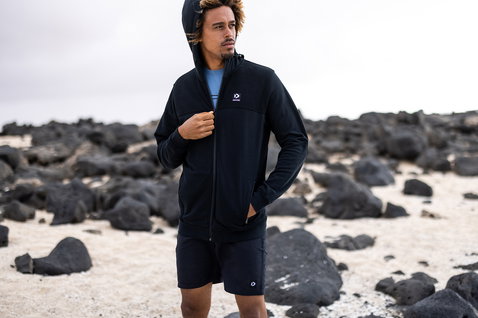 Duotone boardshorts 17 pouces en noir en pose debout sur une plage côtière rocheuse
