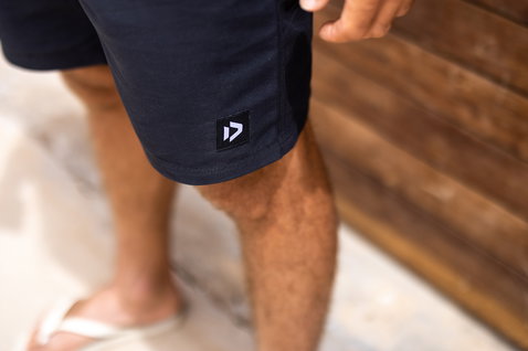 Duotone boardshorts en bleu marine et noir en pose debout sur une terrasse en bois