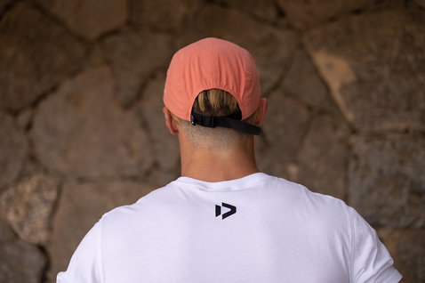 Gorra ajustable en rosa salmón con negro y marrón piedra, usada al aire libre junto a una pared rocosa