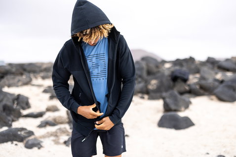 Duotone Zip-Hoodie in schwarzem Marineblau beim Tragen an einem felsigen Vulkanstrand