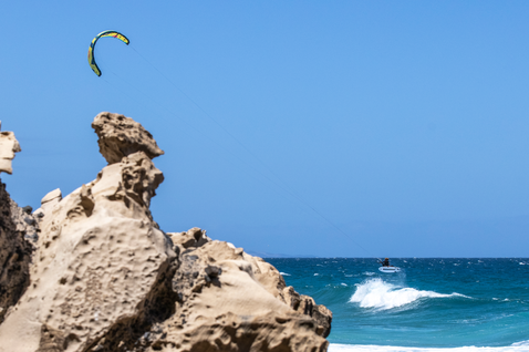 Duotone Fish D/LAB directional kiteboard during wave riding at a rocky coastal beach with open ocean