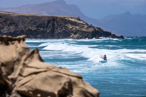Duotone Fish D/LAB directional kiteboard during wave riding at a rocky volcanic coastline
