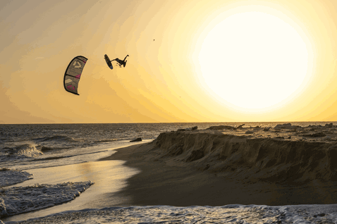 Duotone Whip D/LAB kite surfboard during kitesurfing at the ocean beach with sand cliffs