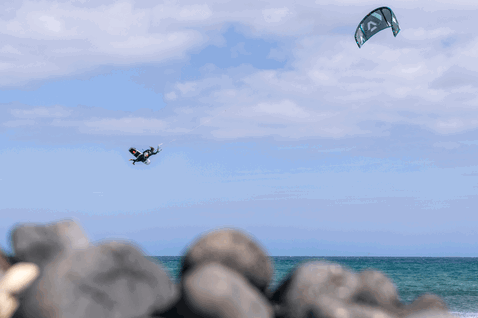 Duotone Neo SLS LEI kite durante el surf de olas en la playa del océano con costa rocosa en gris azulado pizarra, azul acero y azul claro