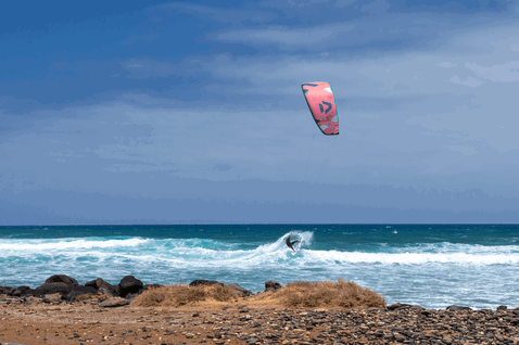 Duotone Neo SLS LEI kite durante el surf de olas en una playa oceánica con costa rocosa