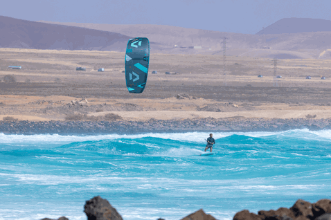 Duotone Neo SLS LEI kite durante el surf de olas en una playa volcánica oceánica
