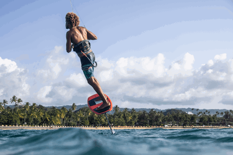Duotone Pace planche de kitesurf foil lors du foiling sur une plage tropicale de l'océan avec palmiers