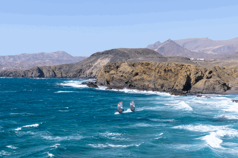 Duotone Rebel SLS LEI kite during kitesurfing at a rocky ocean coastline with mountains