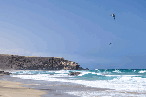 Duotone Rebel SLS LEI kite during kitesurfing at the ocean beach with rocky cliffs