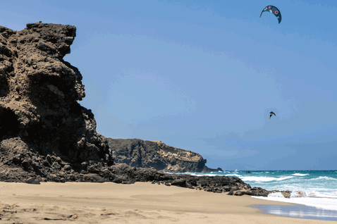 Duotone Rebel SLS LEI kite during kitesurfing at a rocky volcanic beach coastline