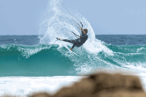 Duotone Whip SLS kite surfboard durante il kitesurf sulla spiaggia oceanica con riva rocciosa