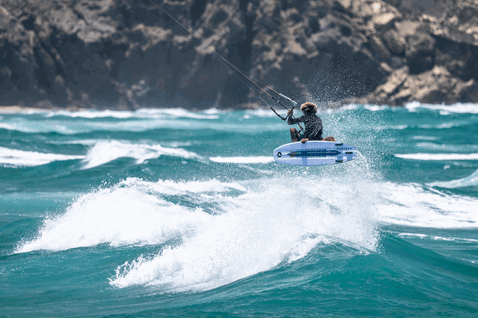 Duotone Whip SLS kite surfboard durante il kitesurf sull'oceano con costa rocciosa