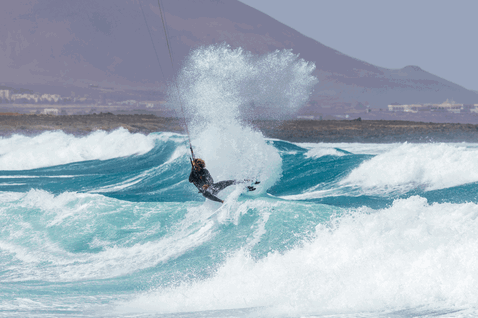 Duotone Whip SLS kite surfboard durante il kitesurf sulla spiaggia con montagne sullo sfondo