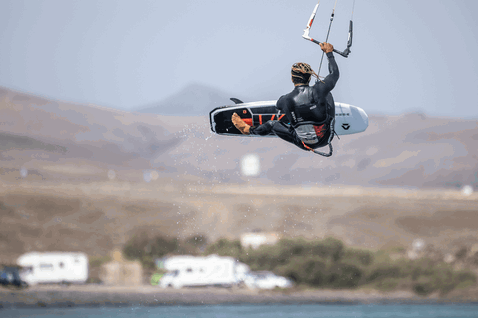 Duotone Voke SLS tabla de kitesurf durante kitesurf en bahía costera con ladera árida de fondo